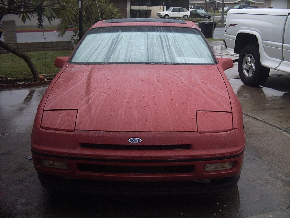 Red first-generation Ford Probe front view, wet from rain, pop-up headlights closed