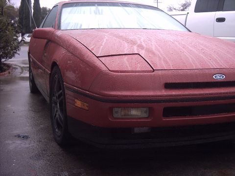 1989 Ford Probe - Front view of a red 1989 Ford Probe on a wet day, showing its distinctive pop-up headlights.