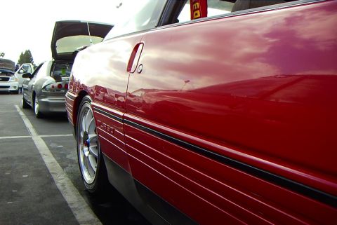 1989 Ford Probe - A red coupe is parked in a lot with other vehicles, focusing on the side panel and wheel.
