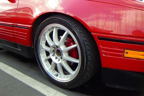 1989 Ford Probe - Close-up of the front wheel and fender of a red 1989 Ford Probe PGT, highlighting its aftermarket wheels and red brake calipers.
