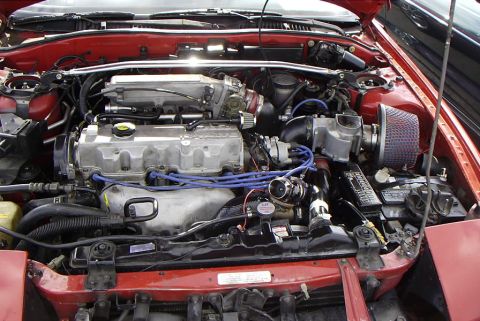 1989 Ford Probe - The engine bay of a red car is shown with various aftermarket modifications and a visible battery.