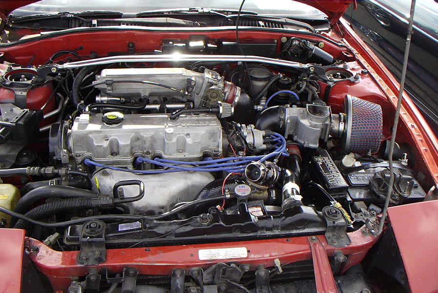 Turbocharged four-cylinder engine bay with blue plug wires and cone air filter in a red car