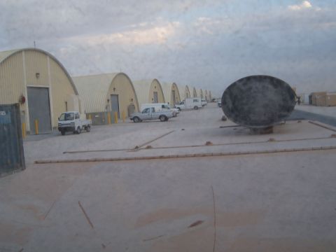 1988 Ford Bronco - A line of quonset huts is visible with several vehicles parked in front, under a cloudy sky.