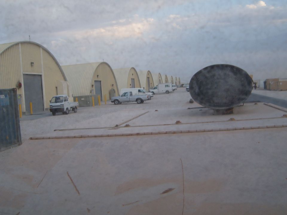 Row of quonset huts with parked vehicles and a large circular object in the foreground