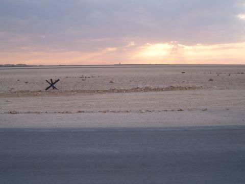 1988 Ford Bronco - Barbed wire and a metal obstacle mark a desolate desert landscape under a cloudy sunset sky.