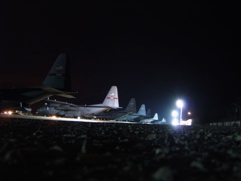1988 Ford Bronco - Military transport planes lined up on a tarmac at night, illuminated by floodlights.