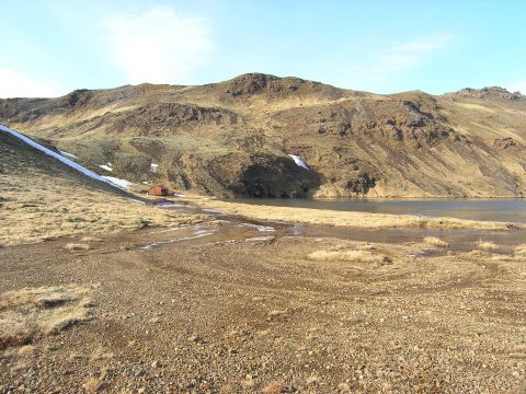 2001 Jeep Wrangler - A remote cabin sits beside a calm lake, surrounded by , dry hills and patches of snow.