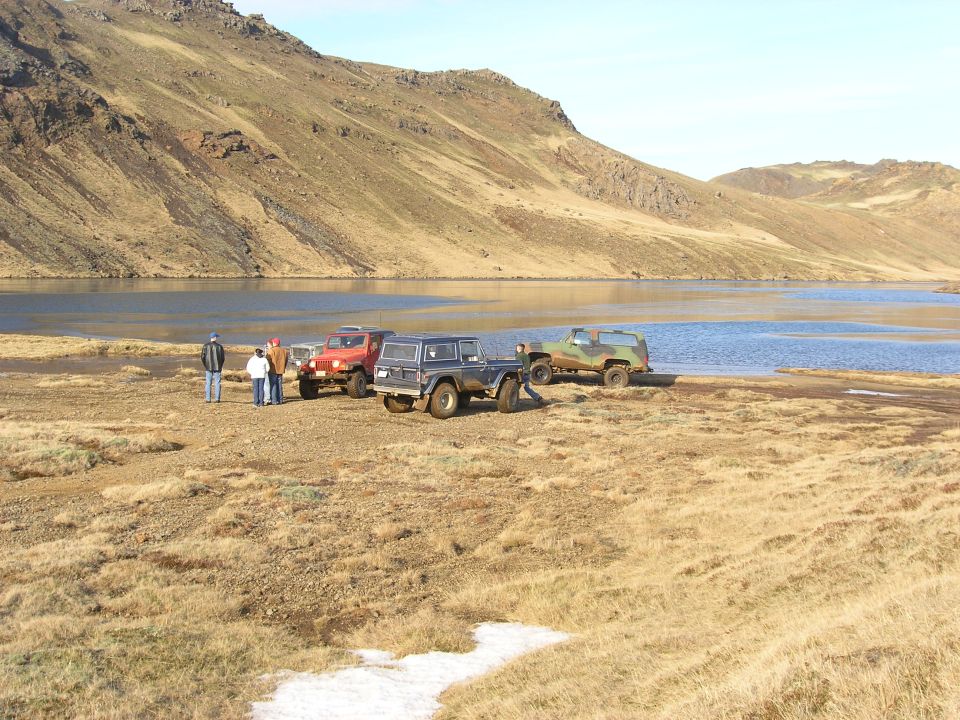 Three off-road vehicles parked by a lake with a mountain in the background