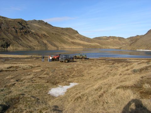 2001 Jeep Wrangler - Several off-road vehicles are parked by a lake in a mountainous, grassy landscape.