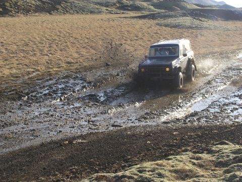 2001 Jeep Wrangler - A dark SUV navigates a muddy track, kicking up water in a barren landscape.