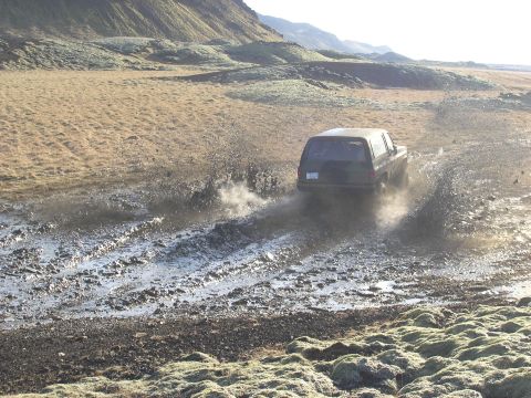 2001 Jeep Wrangler - An SUV navigates a muddy trail, sending water and dirt flying.