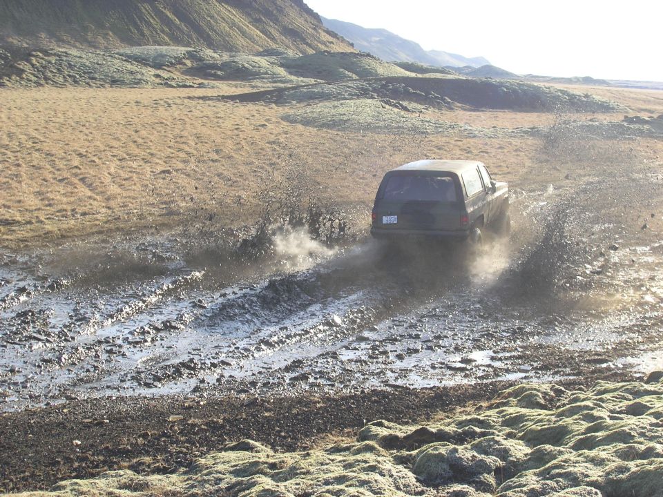 SUV kicking up mud while driving on a dirt track in a barren landscape