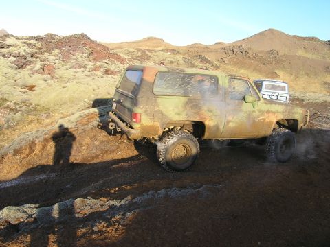 2001 Jeep Wrangler - A camouflaged SUV navigates a , rocky landscape, with another vehicle visible in the distance.