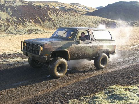2001 Jeep Wrangler - Off-road SUV with camouflage paint and lifted suspension navigates a dusty trail in a barren landscape.