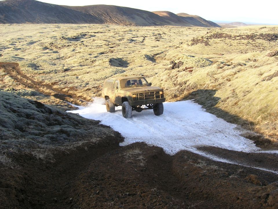 Old Chevy K5 Blazer driving through snow and mud in a barren landscape