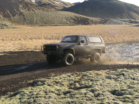2001 Jeep Wrangler - A dark-colored SUV navigates a muddy dirt track through a desolate, mountainous terrain.