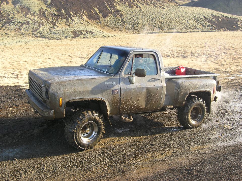 Mud-covered pickup truck with red gas can in bed, off-road tires