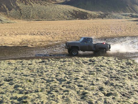 2001 Jeep Wrangler - Pickup truck navigates a wet, off-road terrain with a mountainous backdrop.