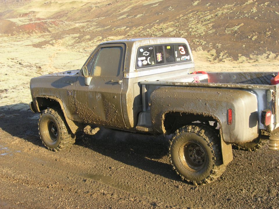 Muddy pickup truck with stickers on the rear window, parked on a dirt road