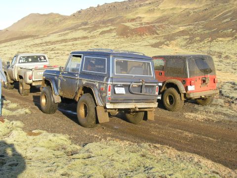 2001 Jeep Wrangler - A dark blue Ford Bronco is seen from the rear, followed by a red Jeep and a pickup truck on a dirt road.