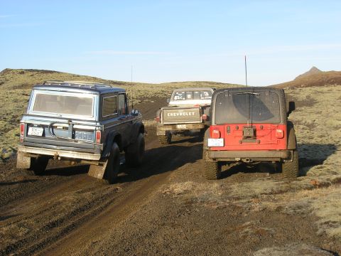 2001 Jeep Wrangler - Three off-road vehicles navigate a muddy track under a clear blue sky.
