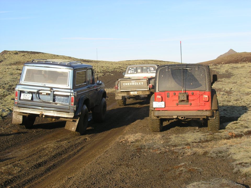Ford Bronco, Chevrolet pickup, and red Jeep Wrangler on a muddy trail