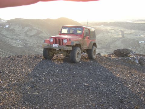 2001 Jeep Wrangler - This red Jeep Wrangler is parked on a rocky, barren landscape under a bright sky.