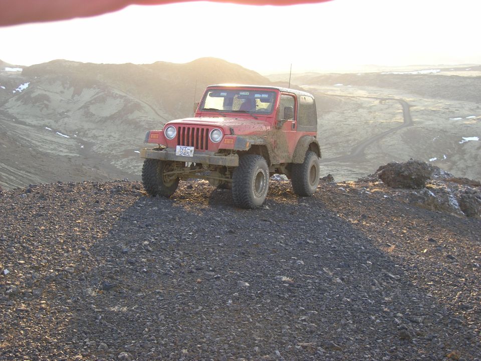 Red Jeep Wrangler parked on a rocky hill with a mountainous background