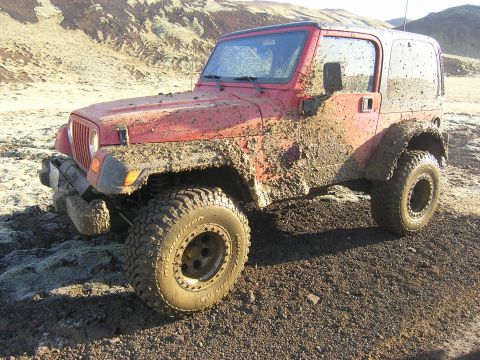 2001 Jeep Wrangler - This red Jeep TJ, coated in mud, is captured in a 3/4 front view, suggesting it has been used for off-roading.