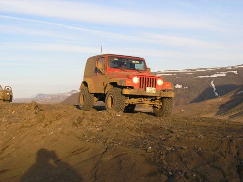 2001 Jeep Wrangler - A red Jeep Wrangler navigates a rocky, off-road terrain under a clear sky.