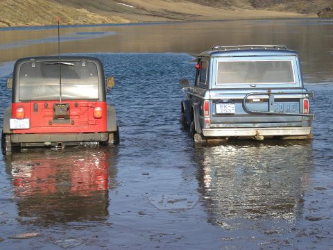 2001 Jeep Wrangler - Two 4x4 vehicles are partially submerged in a body of water with a hilly landscape in the background.