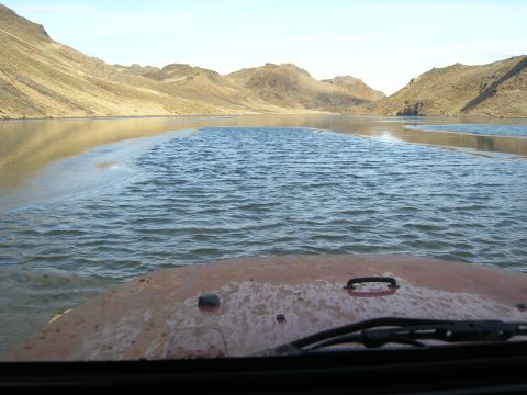 2001 Jeep Wrangler - A 2001 Jeep TJ navigates a shallow water crossing, with arid mountains and a calm lake surrounding the path.