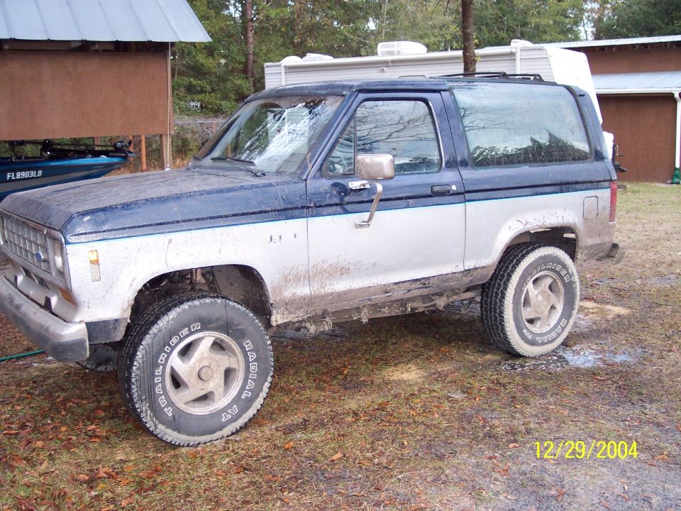 Two-tone blue and white Ford Bronco II parked in a muddy yard