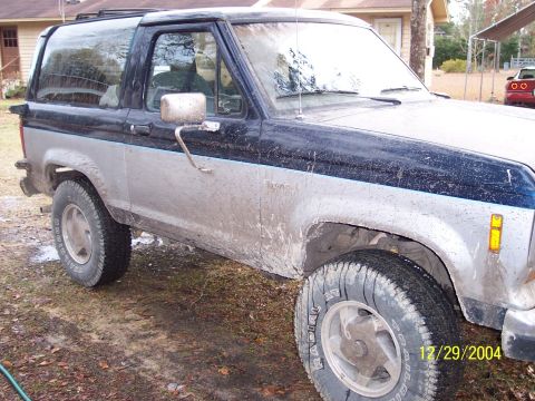 1993 Ford Bronco - This 1993 Ford Bronco, seen in a 3/4 front view, is heavily covered in mud, suggesting recent off-road use.