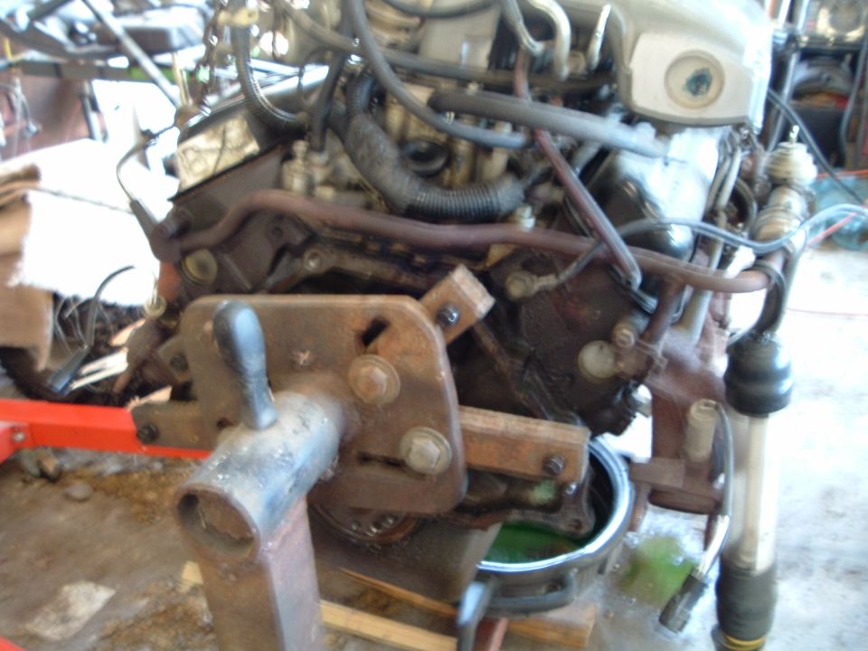 Engine on a stand, with hoses and metal parts visible. Green fluid in a pan below