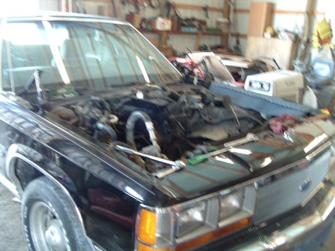1989 Ford Crown Victoria LTD - The engine bay of a black 1989 Ford Crown Victoria LTD is open for service in a garage.