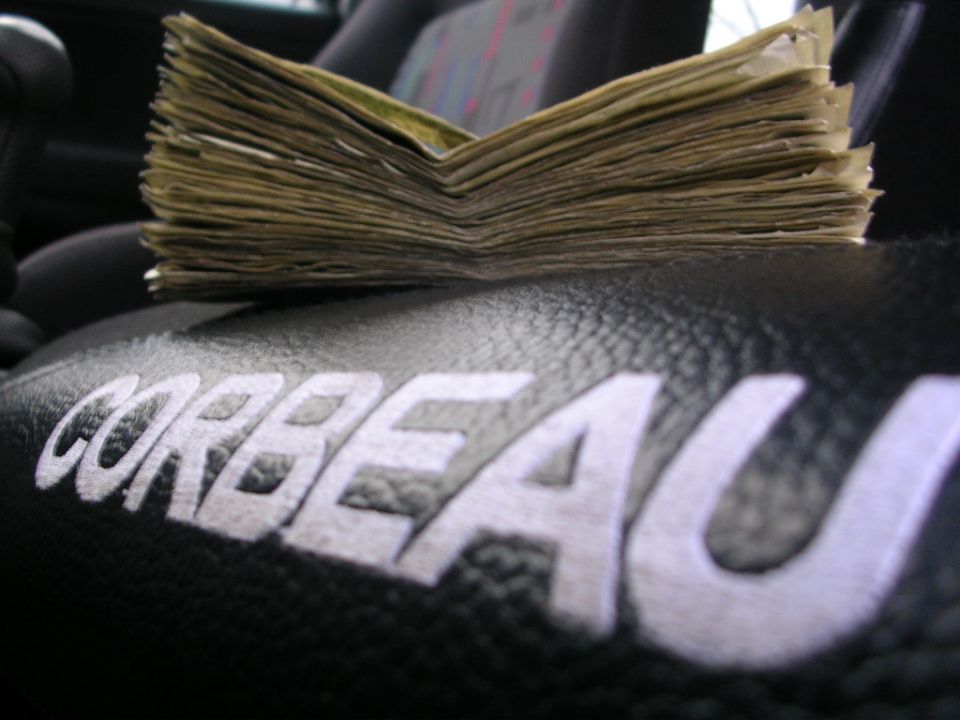 Stack of cash on a Corbeau racing seat. Supermotors.net logo visible