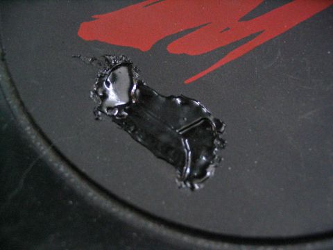 1993 Ford Taurus - Close-up of black sealant applied to a damaged area on a black surface with a red graphic, showing a Supermotors.net watermark.