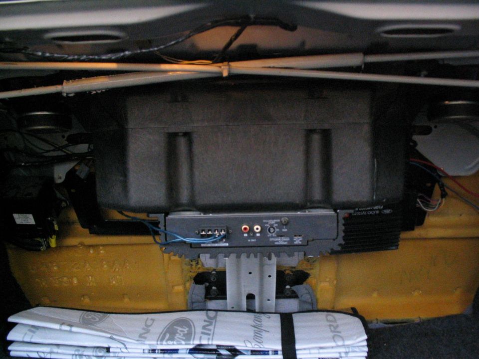 Amplifier and subwoofer enclosure mounted in a car trunk against a yellow rear bulkhead