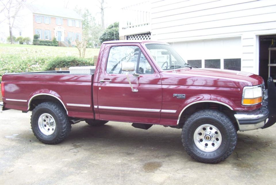 Burgundy Ford F-150 regular cab pickup, passenger side, on lifted all-terrain tires in a driveway