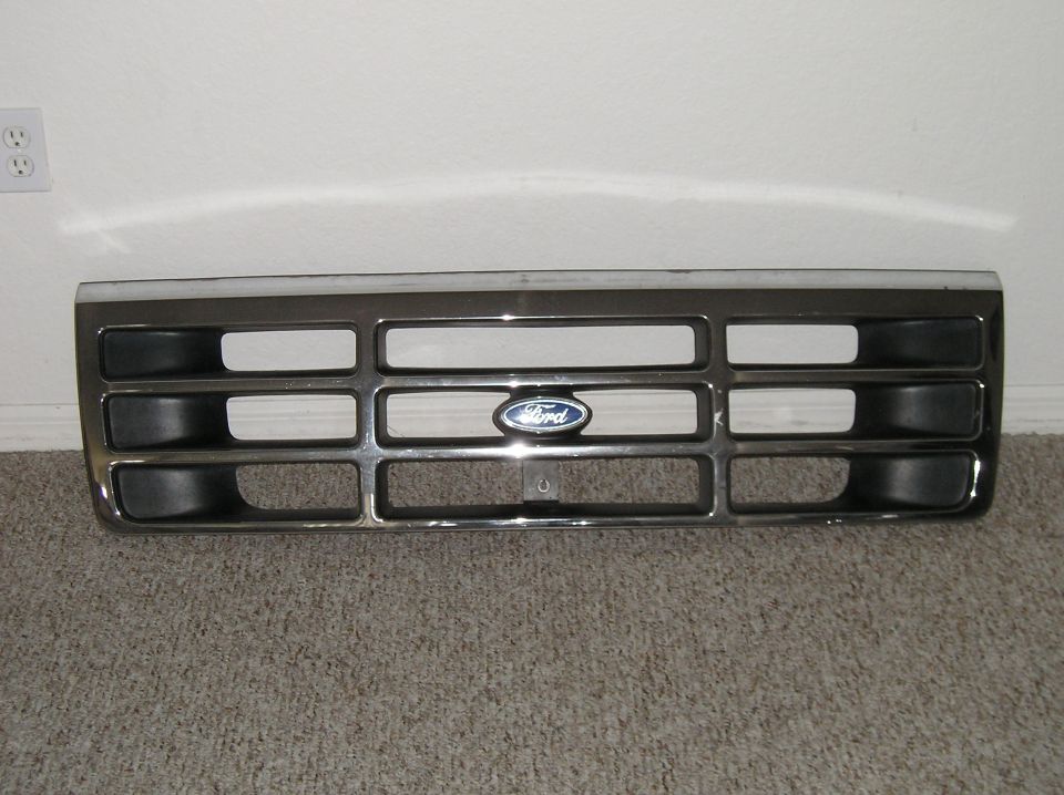 Chrome Ford grille with blue oval emblem leaning against a white wall on carpet