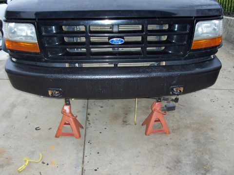 1994 Ford F-150 - The front of a black Ford truck is elevated on jack stands, displaying its grille and a textured bumper.