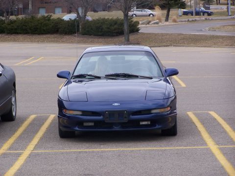 1993 Ford Probe - A blue 1993 Ford Probe is parked head-on in a parking lot with its headlights up.