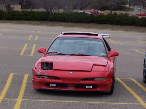 1993 Ford Probe - A red 1993 Ford Probe is parked in a lot, showing damage to its front end and a prominent rear spoiler.