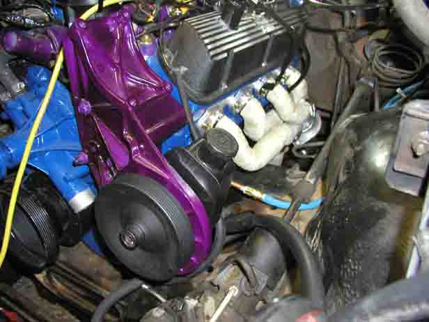 Engine bay with a shiny purple power steering pump bracket and other engine components