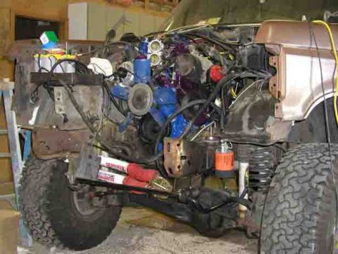 1988 Ford Bronco - Front end of a 1988 Ford Bronco undergoing engine work, showing suspension components and wiring.