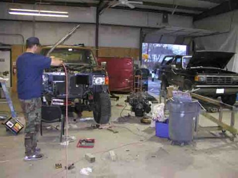 1988 Ford Bronco - Mechanic works on a 1988 Ford Bronco in a garage; another Bronco is parked in the background.