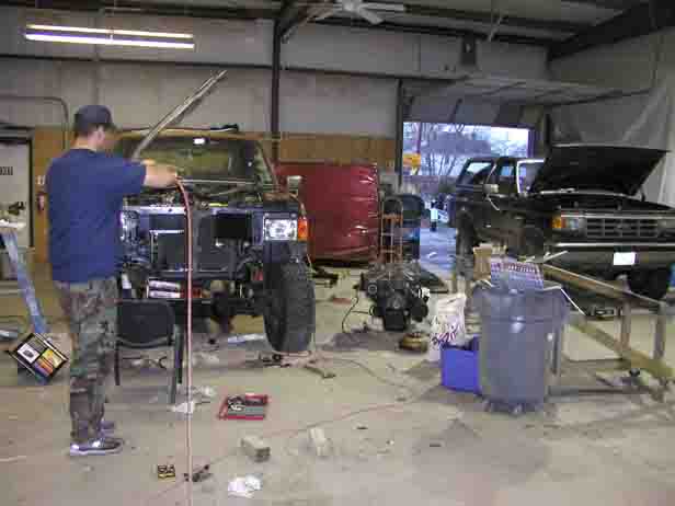 1988 Ford Bronco with front end disassembled in a garage, another Bronco visible in background