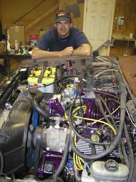 1988 Ford Bronco - Man leans over a custom engine bay with purple accents and dual batteries.