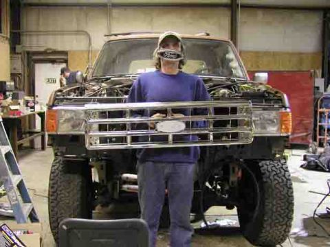 1988 Ford Bronco - Man holds a Ford grille in front of a 1988 Ford Bronco during installation.